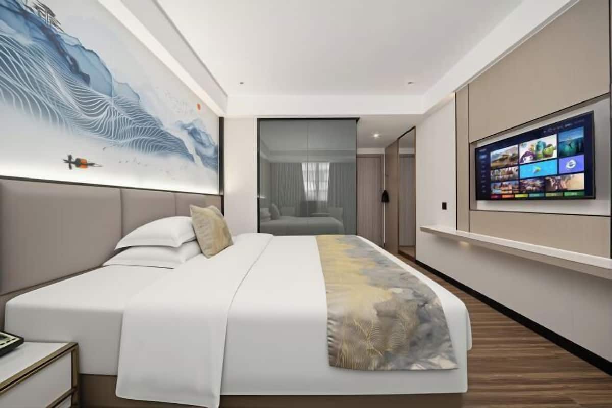 A modern hotel room with a large bed, a TV on the wall, and a painting above the bed.