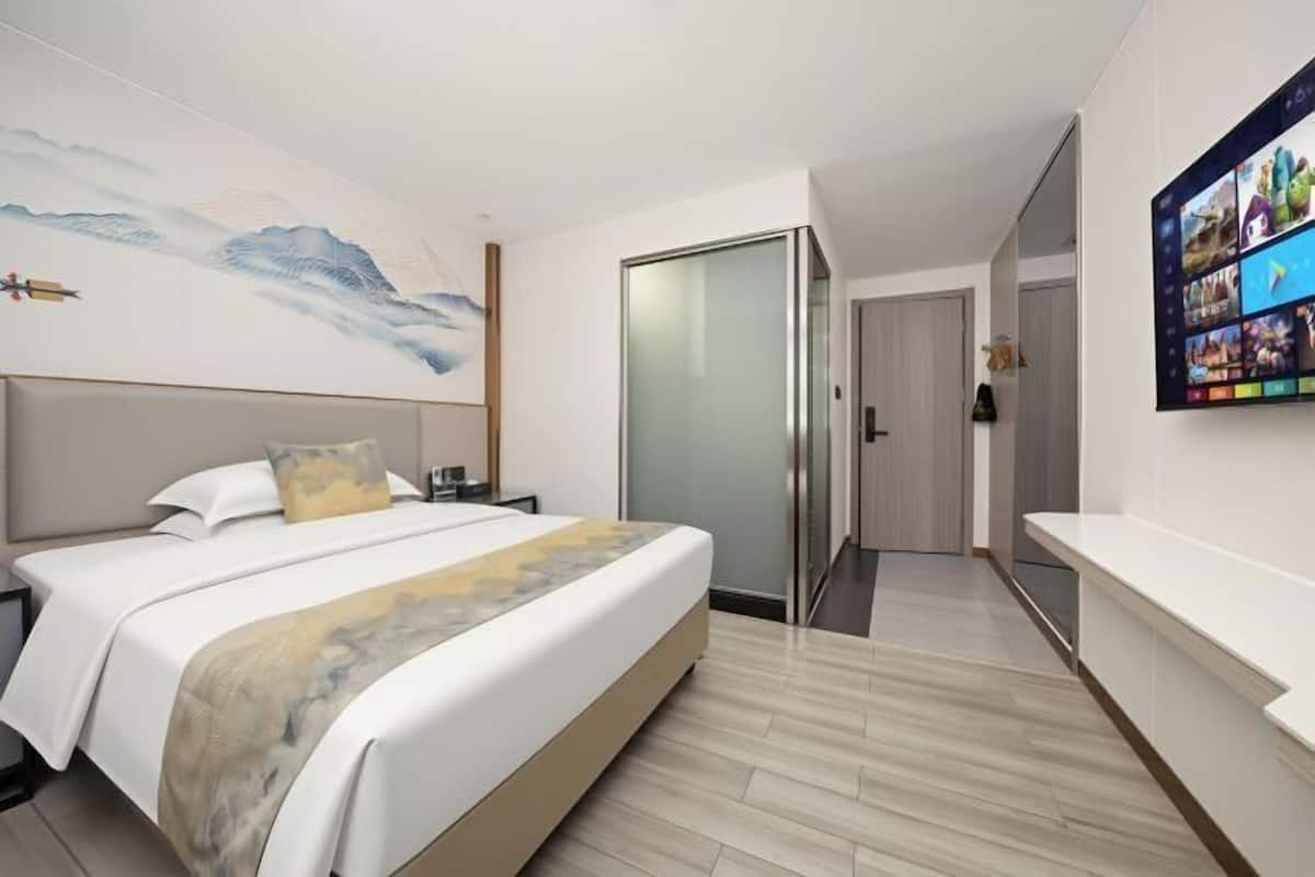A hotel room with a bed, a TV, a painting on the wall, and a sliding door.