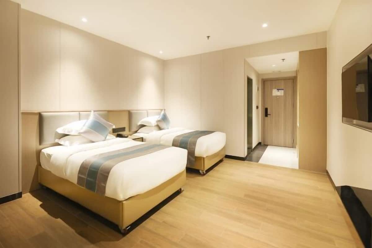 A hotel room with two beds, a flat-screen TV, and a wooden floor.