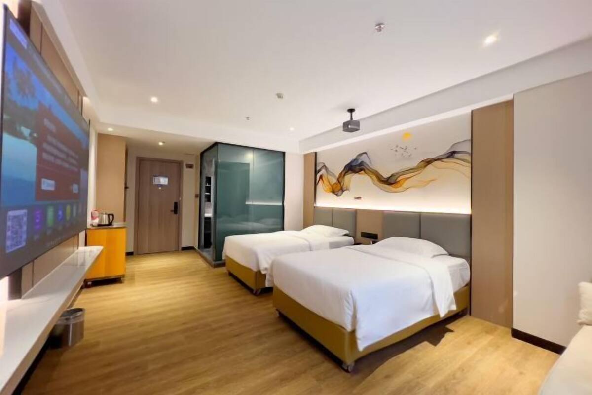 A hotel room with two beds, a TV, a wall art piece, and a wooden floor.
