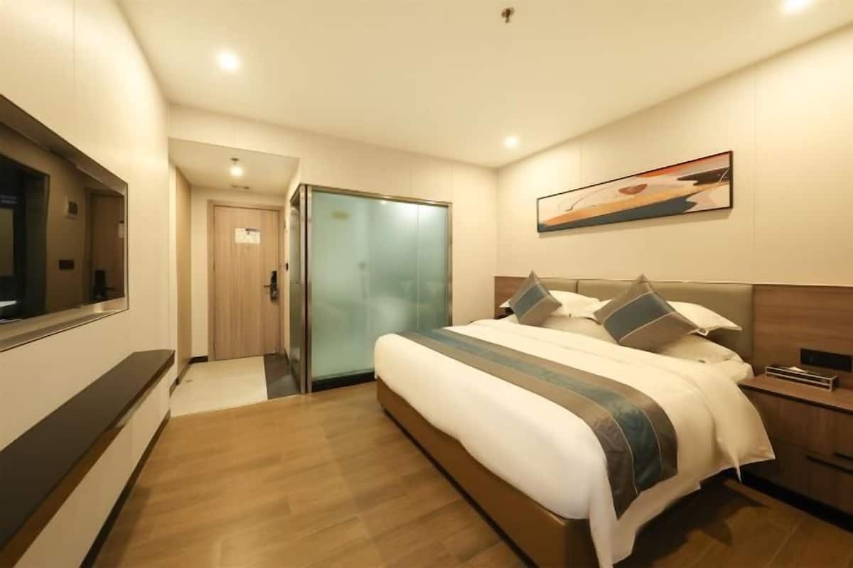 A modern hotel room with a large bed, a television, a glass door closet, and a painting on the wall.