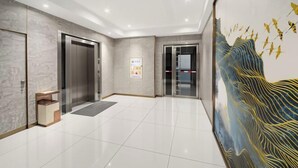 A modern hotel lobby with a marble floor, elevators, a reception desk, and a large wall mural. - Jiangmen ParkLane Hotel (Xiangshan Park Xinqiao Branch) (Jiangmen)