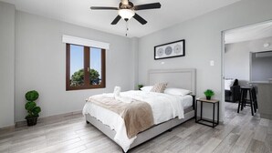 A modern bedroom with a bed, a ceiling fan, a window, and a small table with a plant. - VelBELA Rincon (Rincon)