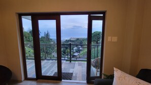 A room with a large sliding glass door leading to an outdoor balcony with a view of a hilly landscape and a body of water. - VelBELA Rincon (Rincon)