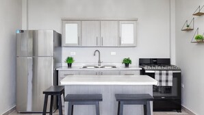 A modern kitchen with a stainless steel refrigerator, a gas stove, and a built-in oven. There are two bar stools and two potted plants on the counter. - VelBELA Rincon (Rincon)