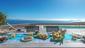 A breakfast setup with a view of the sea, including plates of food, glasses of juice, and a table with a blue tablecloth. - Tranquil sea view villa with pool,2km from beach! (Agia Galini)
