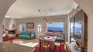 A spacious living room with a fireplace, a dining area, and a large window offering a view of the sea. - Tranquil sea view villa with pool,2km from beach! (Agia Galini)