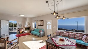 A spacious living room with a sofa, dining table, and a large window overlooking the sea. - Tranquil sea view villa with pool,2km from beach! (Agia Galini)
