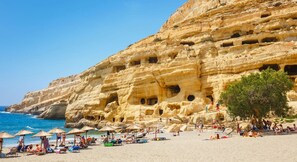 A beach with a rocky cliff featuring multiple caves and a clear blue sky. - Tranquil sea view villa with pool,2km from beach! (Agia Galini)