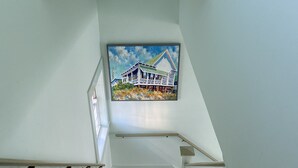 A wooden staircase with white walls and a painting of a house and flowers on the wall above it.