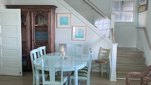 A dining area with a round table and chairs, a ceiling fan, a staircase, and a door leading to another room.