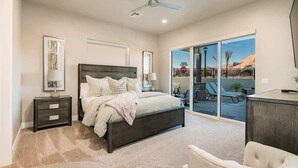 Une chambre à coucher comprenant un lit, des tables de chevet, un ventilateur de plafond et une vue sur l’extérieur grâce à de grandes portes-fenêtres coulissantes.