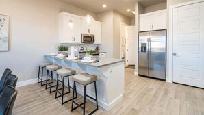 Una cocina moderna con armarios blancos, un refrigerador de acero inoxidable y una isla central con taburetes de bar.