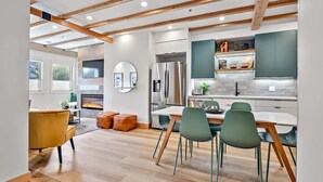A modern kitchen with wooden beams, a large refrigerator, and a dining area with green chairs. - Raven's Nest - Perfectly Located on Main Street (Canmore)