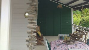 A covered outdoor seating area with a table and chairs, a green door, and a hanging light fixture. - LES FLAMBOYANTS LA PETITE MAISON CRÉOLE (Anse-Bertrand)