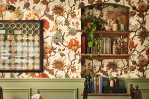 Een kamer met bloemenbehang, een lijst met antieke flessen en een boekenplank met boeken en decoratieve objecten.