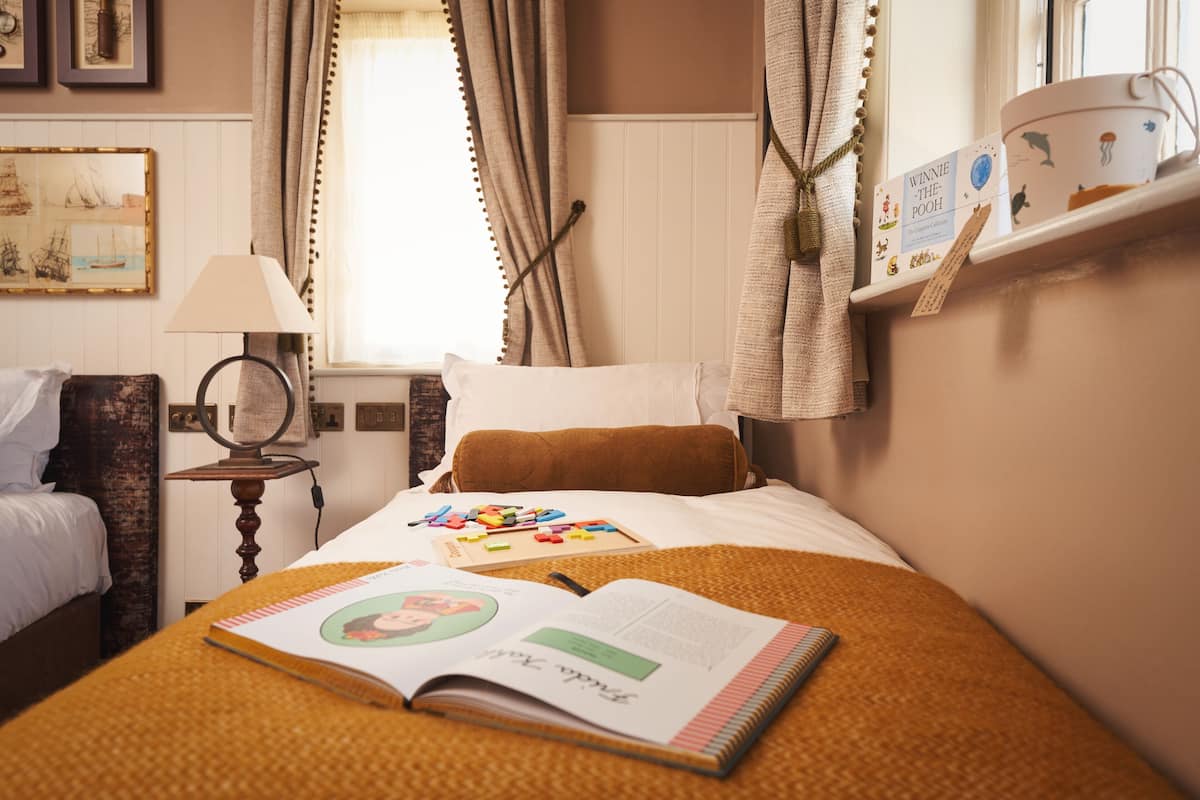 Cama bem arrumada com um livro, brinquedos, abajur e janela com cortinas.