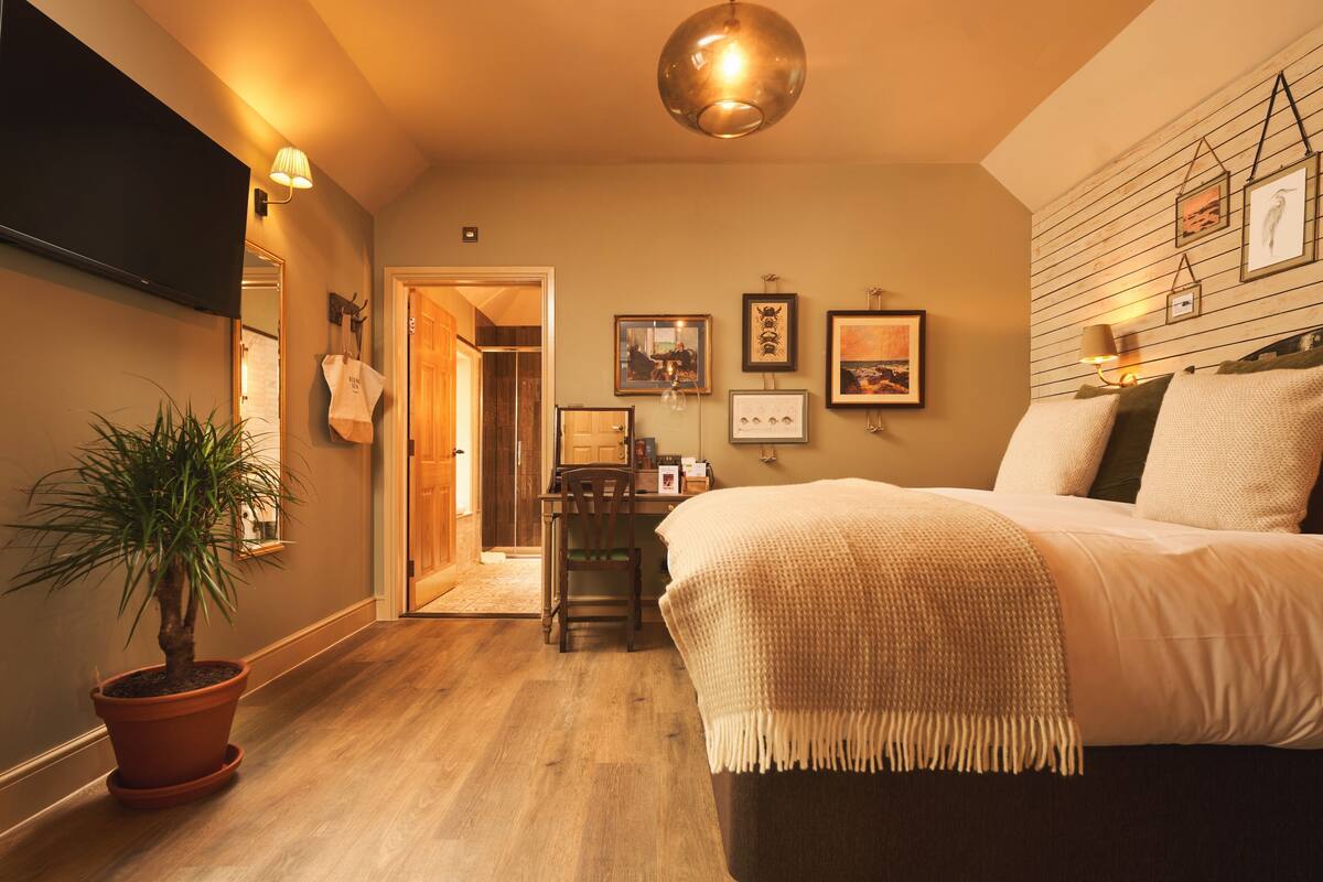Quarto com cama, mesa de cabeceira, luminária e obra de arte na parede.