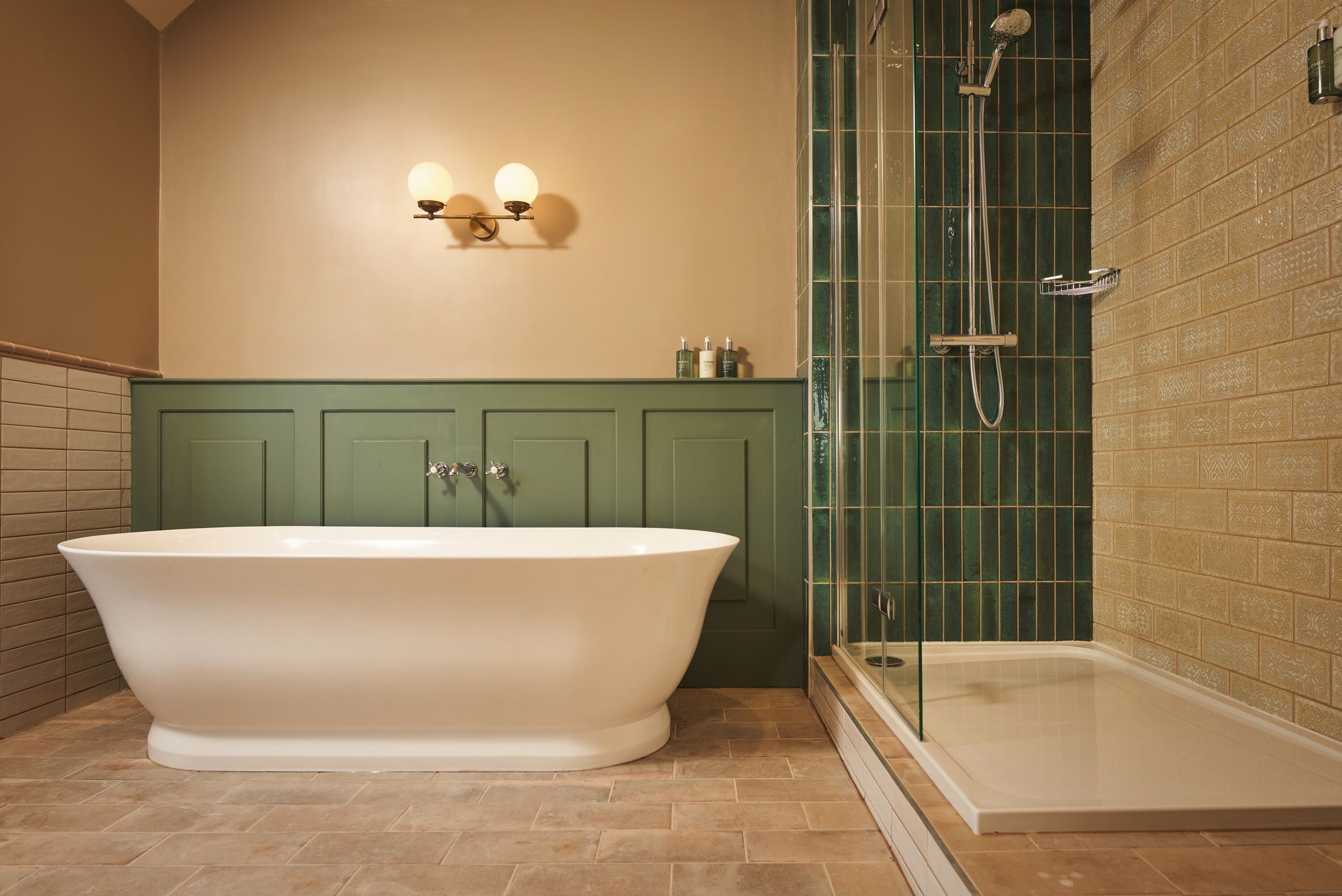 A bathroom with a freestanding bathtub, a glass-enclosed shower, and a green vanity with two wall-mounted lights.