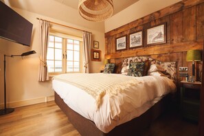 A bedroom with a large bed, wooden headboard, framed pictures, a window with curtains, and a floor lamp. - The Rising Sun (Truro)