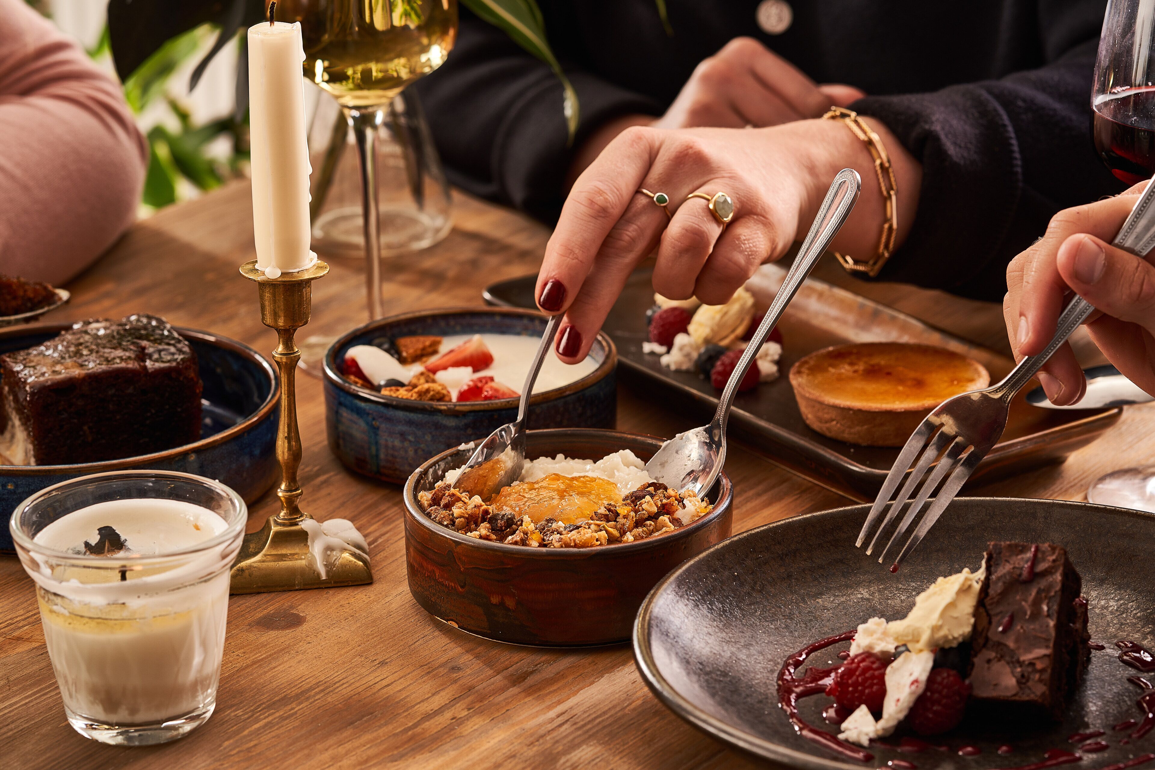 A dining table with various dishes, including a dessert with berries and chocolate, a bowl of nuts, and a glass of white wine.