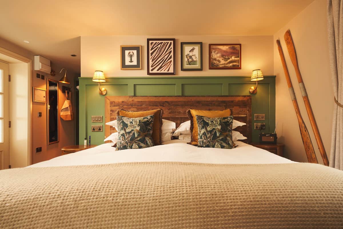 A neatly made bed with floral pillows, a green headboard, and wall-mounted lamps.
