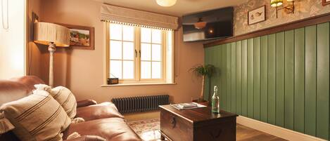 Una sala de estar con un sofá de cuero marrón, una mesa de centro de madera, un radiador, una pared verde con paneles y una ventana con cortina blanca.