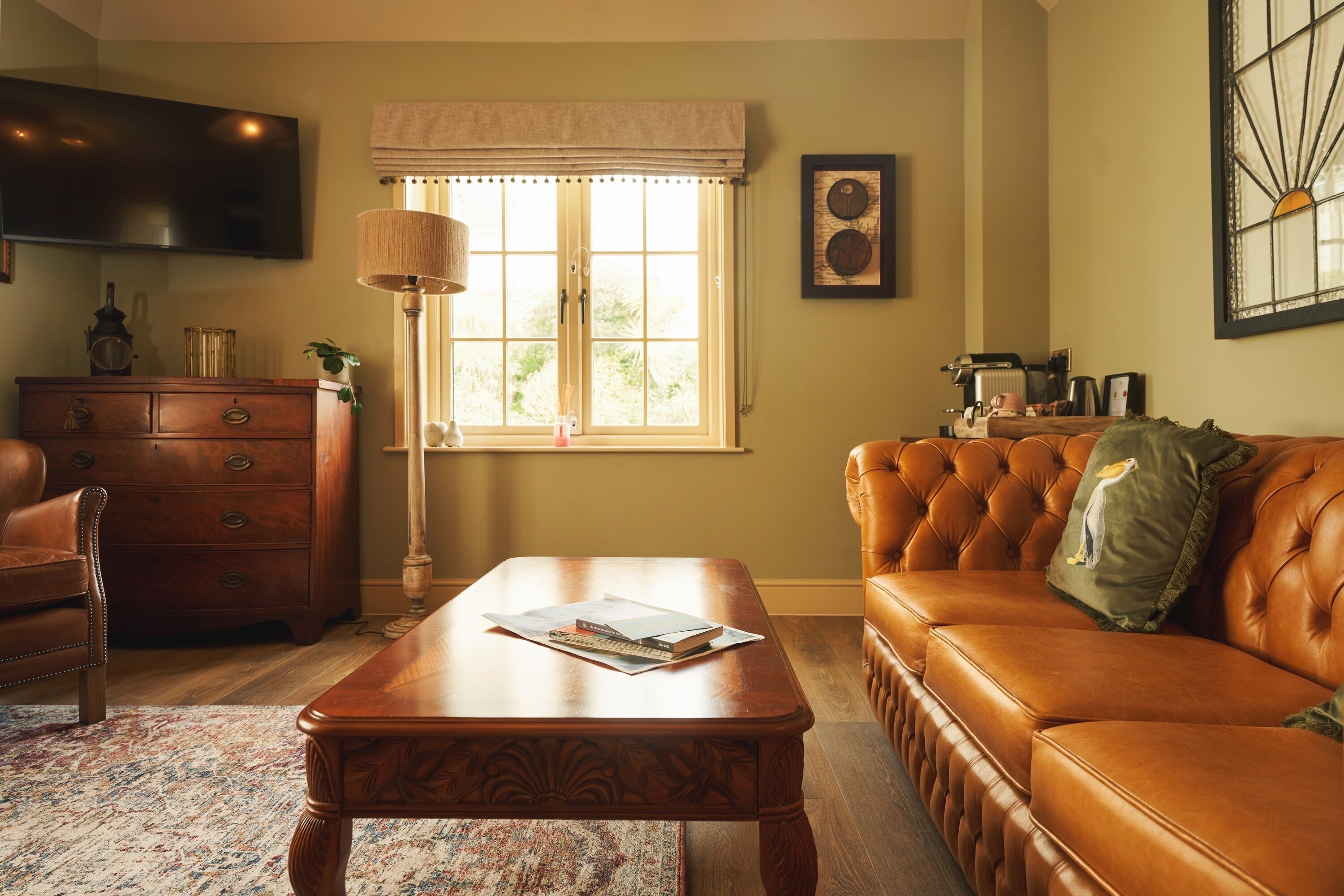 A living room with a wooden coffee table, a leather sofa, a wooden cabinet, and a window with a view of greenery.