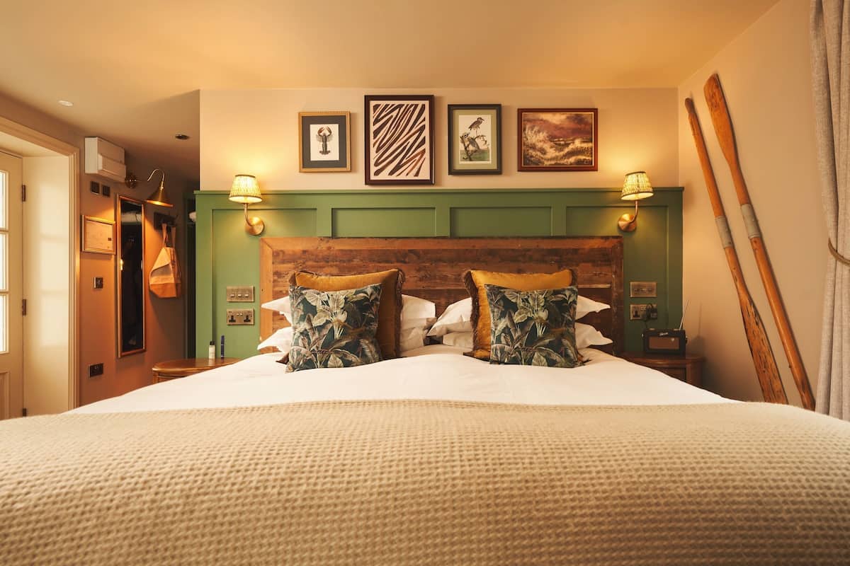 Cama bem arrumada com almofadas florais, cabeceira de madeira e obra de arte na parede.