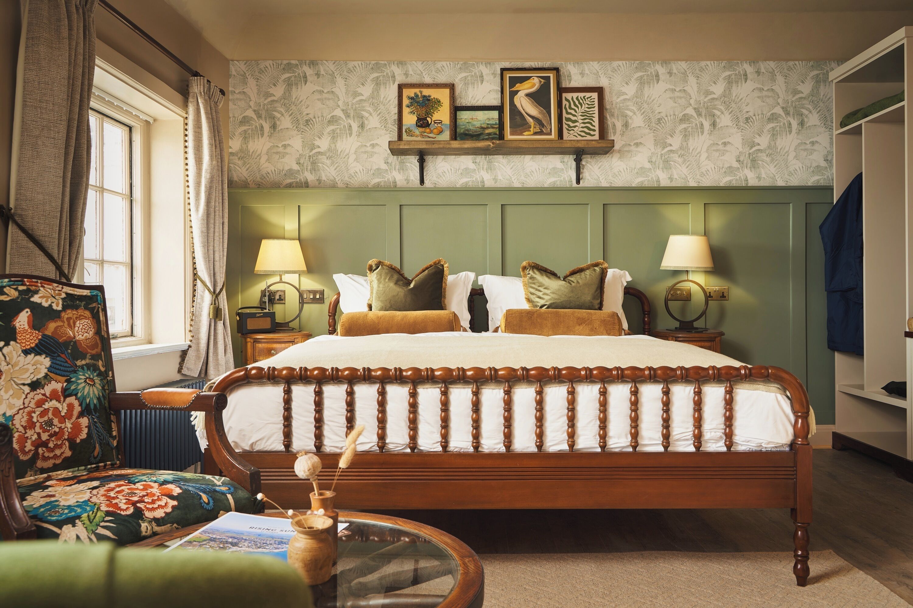 Una camera da letto tradizionale con un letto a baldacchino, due lampade ai comodini, una poltrona con motivo floreale e un poggiatesta verde.