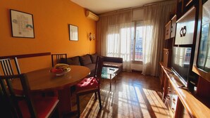 A living room with a wooden dining table, chairs, a sofa, and a TV. - Plaza Universitat Apartment (Barcelona)