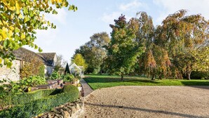 A gravel driveway leading to a stone wall with a hedge.