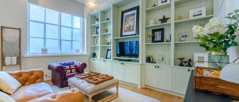 A living room with a leather sofa, a red and blue armchair, a television, and a bookshelf with various items.