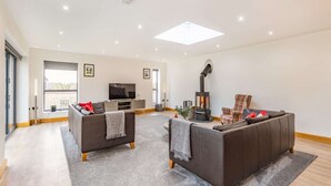 A spacious living room with a large sofa set, a television, a fireplace, and a balcony with a view. - Three bedroom dog friendly holiday home in the Cotswolds - The New Bakehouse (Stroud)