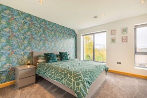 A bedroom with a large bed, a nightstand, a dresser, and a window with a view. - Three bedroom dog friendly holiday home in the Cotswolds - The New Bakehouse (Stroud)