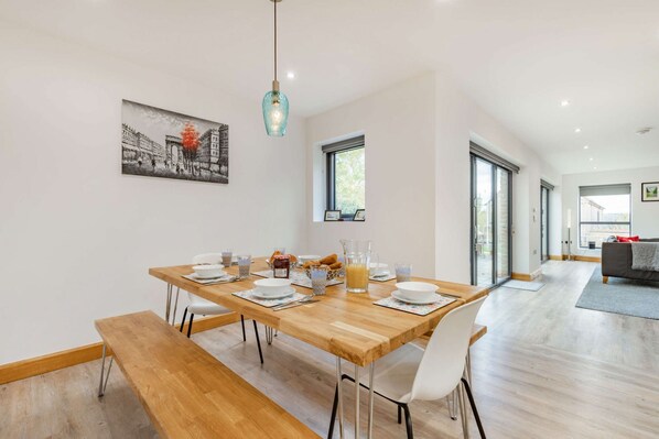 A dining area with a wooden table set for breakfast, a bench, and a modern pendant light.