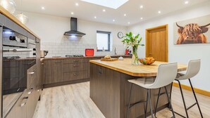 A modern kitchen with a skylight, wooden cabinets, and a central island with bar stools. - Three bedroom dog friendly holiday home in the Cotswolds - The New Bakehouse (Stroud)