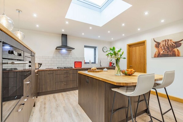 A modern kitchen with a skylight, wooden cabinets, and a central island with bar stools.