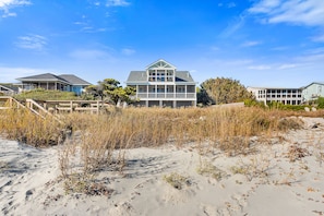 A beachfront property with a large house featuring a wrap-around porch and multiple windows.