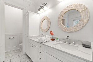 Uma casa de banho moderna com um lavatório branco, dois espelhos redondos, uma decoração de flamingo vermelho e uma sanita branca.