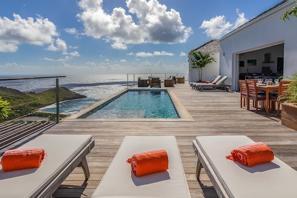 Relax by the ocean with a dip in the pool, surrounded by lounge chairs and a dining area.