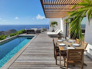 A wooden deck with a pool, lounge chairs, and a table set for dining, overlooking a scenic ocean view. - Villa La Vue (1 bedroom) (Saint Barthélemy)
