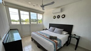 Een slaapkamer met een bed, een plafondventilator, een raam en een klein tafeltje.
