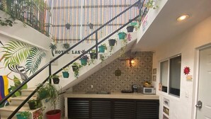Een hotel lobby met een trap, planten in potten, een magnetron en een klein aanrecht.
