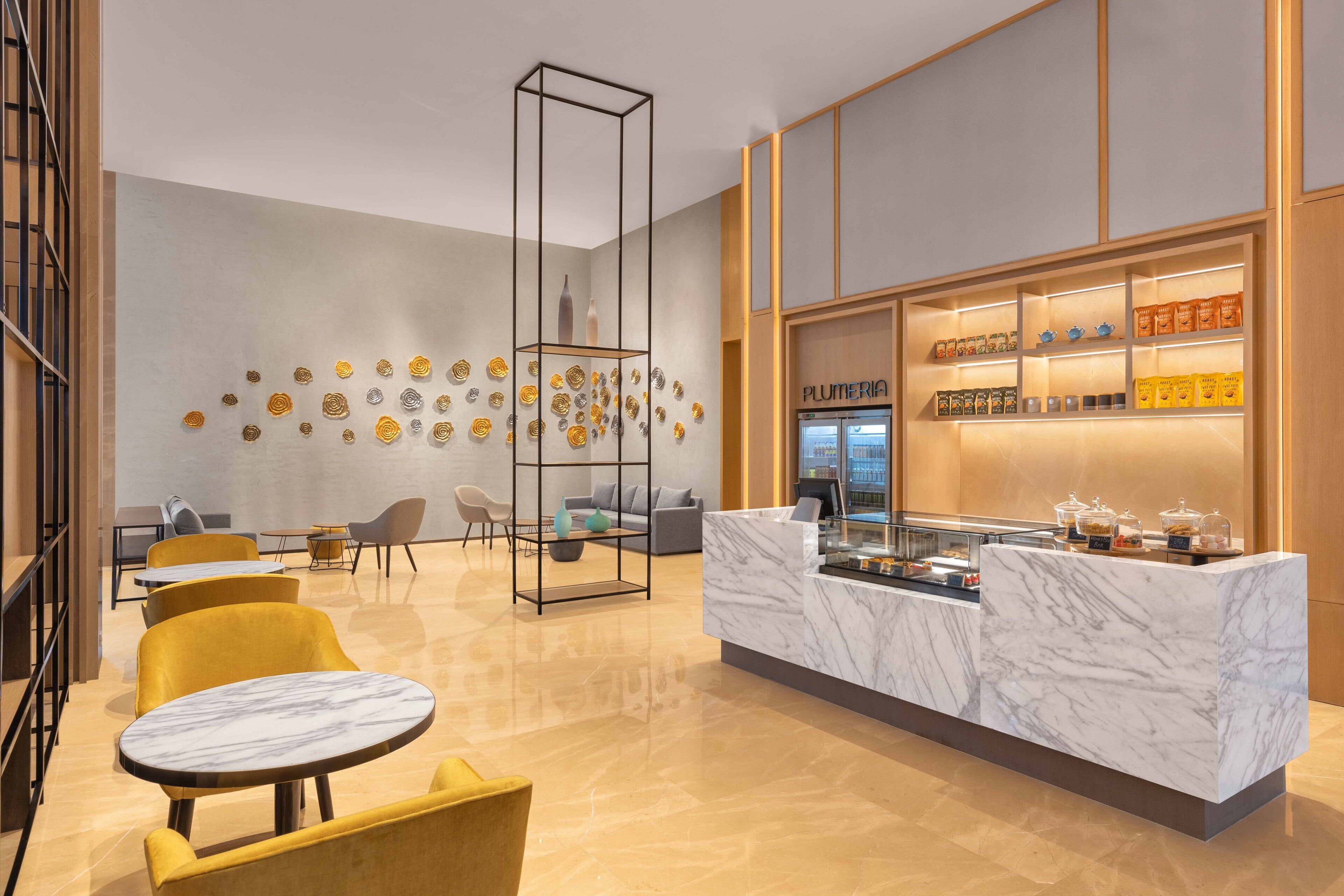 A modern lobby with a marble reception desk, yellow chairs, and a coffee station.