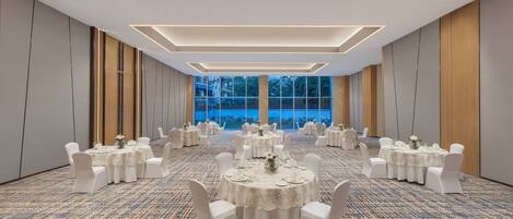 Un amplio salón de banquetes con varias mesas redondas, cada una con sillas blancas y completa con lo necesario.