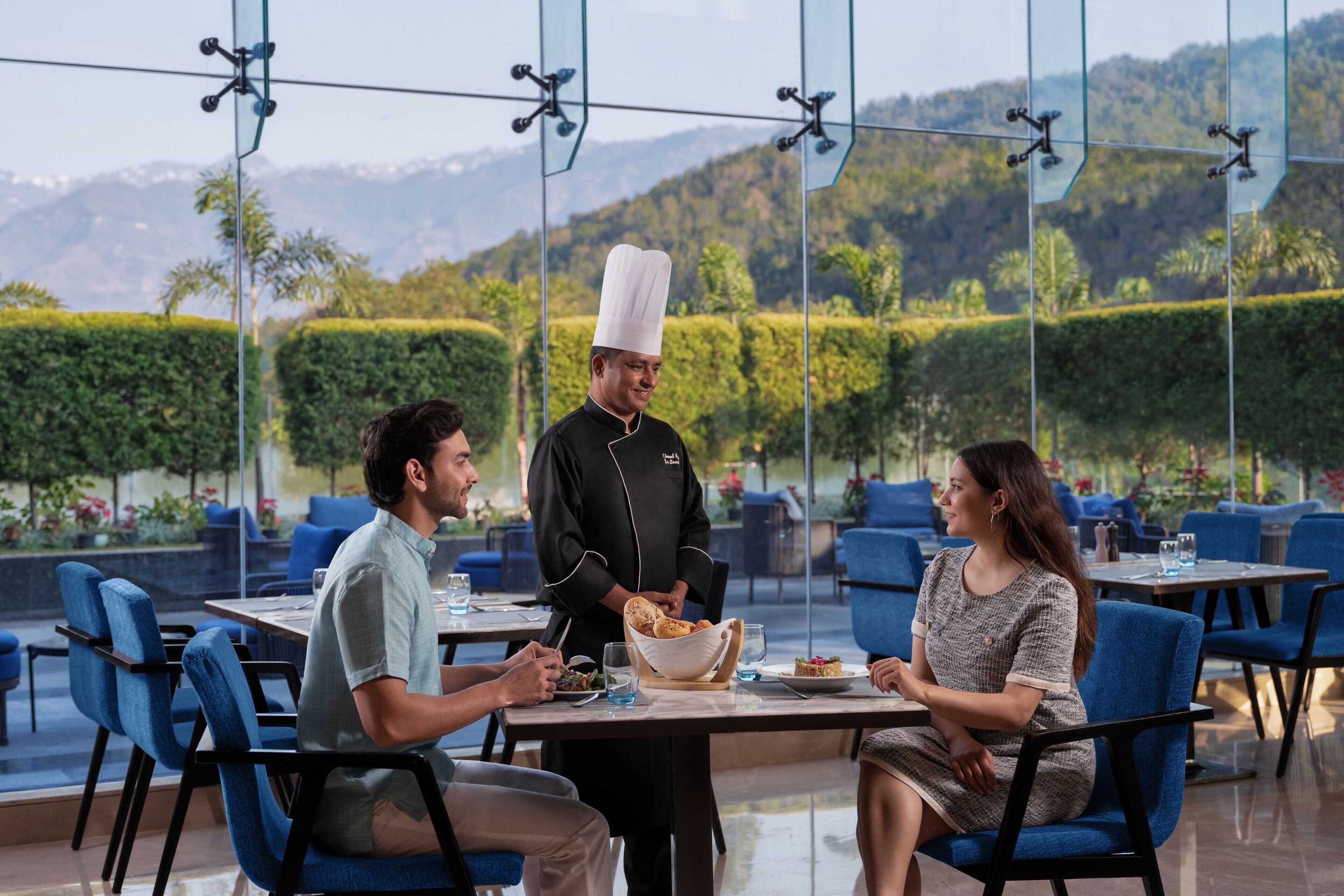 Un restaurant avec une terrasse, un serveur qui apporte les plats et une vue magnifique sur les montagnes.