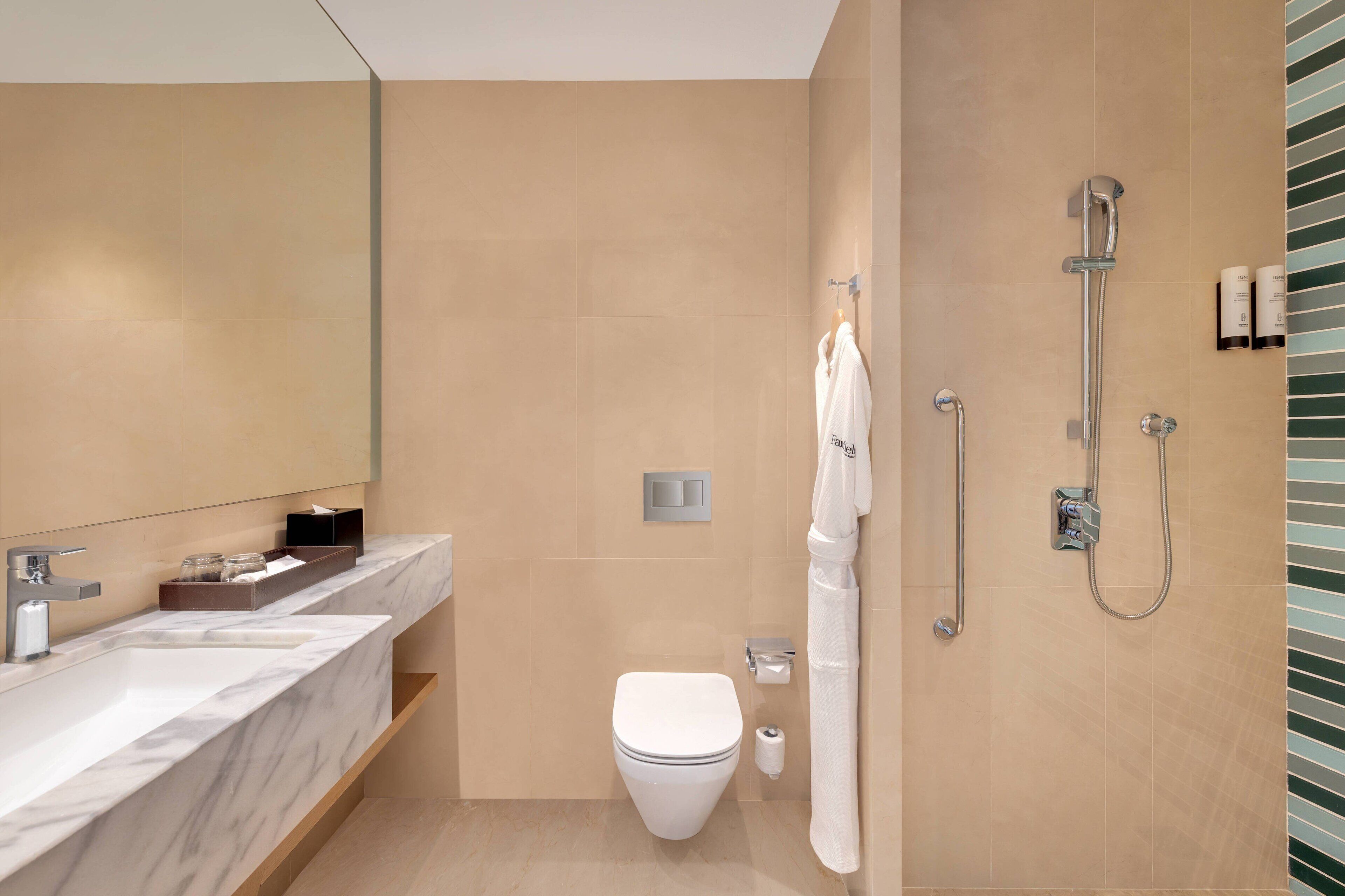Une salle de bain moderne avec un lavabo en marbre, des toilettes et une douche à l’italienne.
