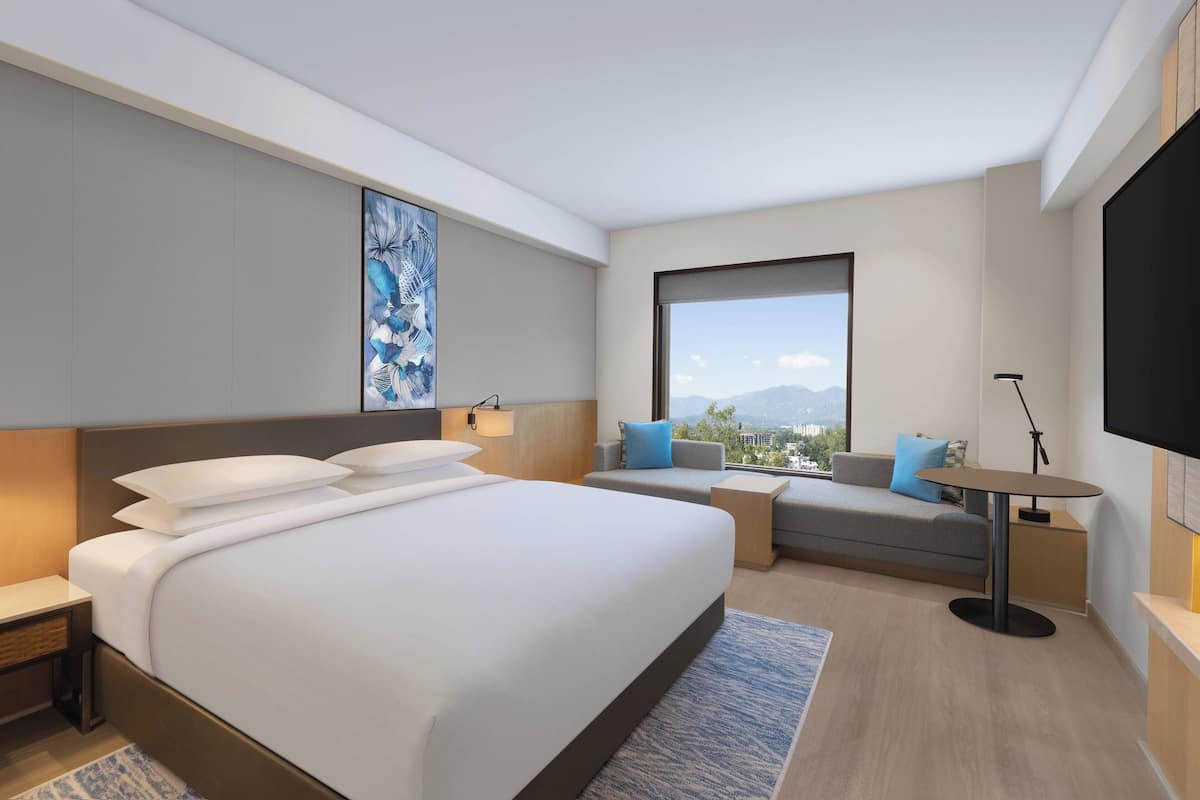 A modern hotel room with a large bed, a sofa, a small table, and a TV.