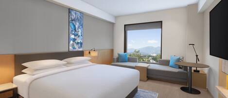 A modern hotel room with a large bed, a sofa, a small table, and a TV.